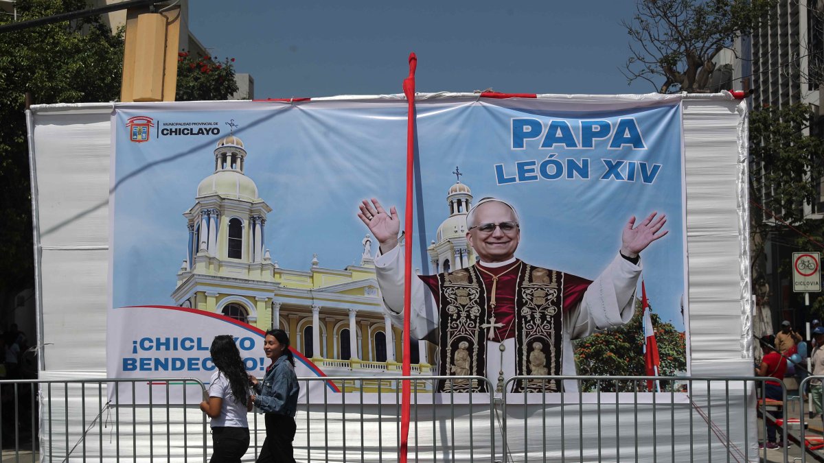  Personas pasan frente a una pancarta con la imagen del papa León XIV este sábado, en la Plaza de Armas en Chiclayo (Péru). 