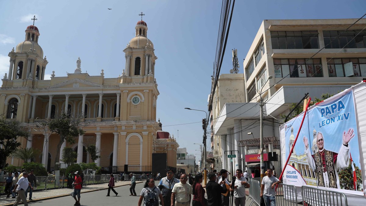 Personas pasan frente a una pancarta con la imagen del papa León XIV en la Plaza de Armas en Chiclayo (Péru).