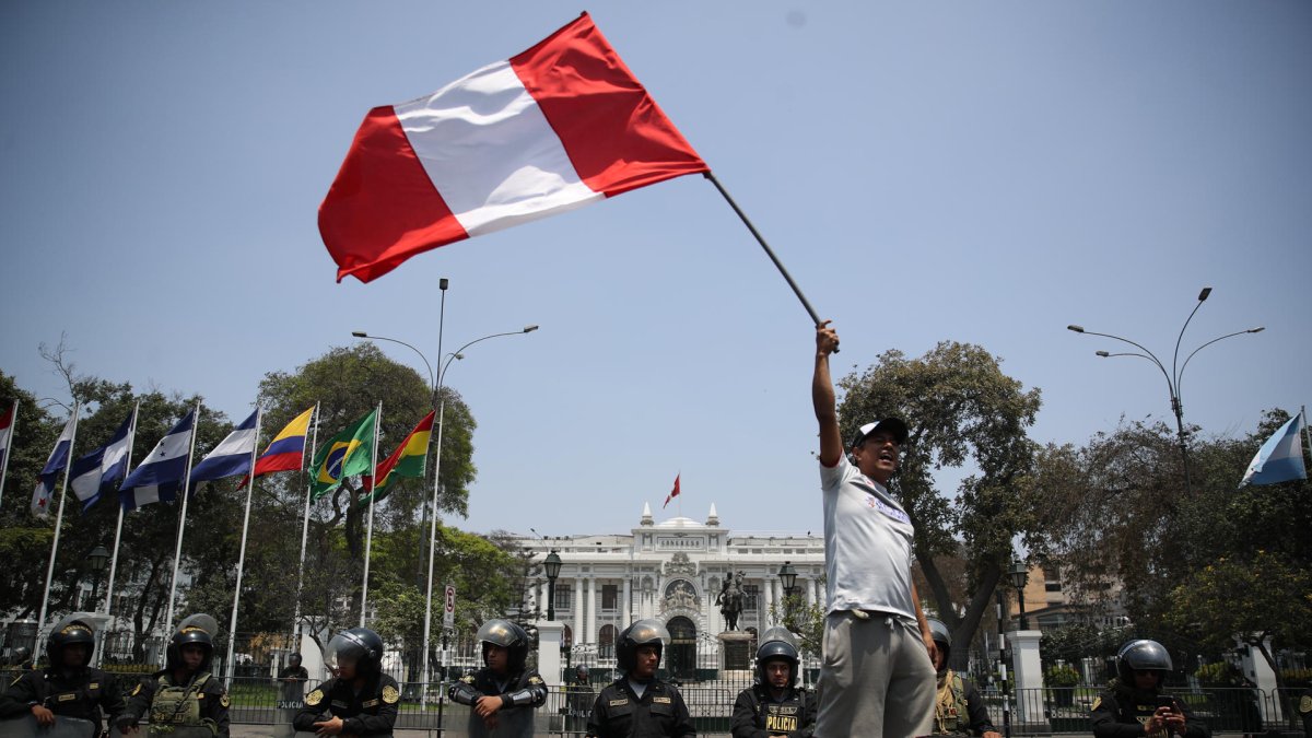 Fotografía de un hombre al ondear una bandera peruana, frente a la sede del Congreso Nacional de Perú, en Lima (Perú).
