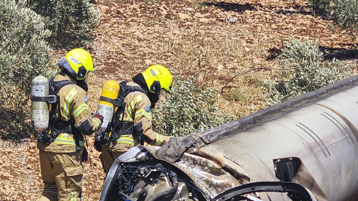 Dos bomberos observan los restos de un misil balístico iraní en un olivar de Galilea.