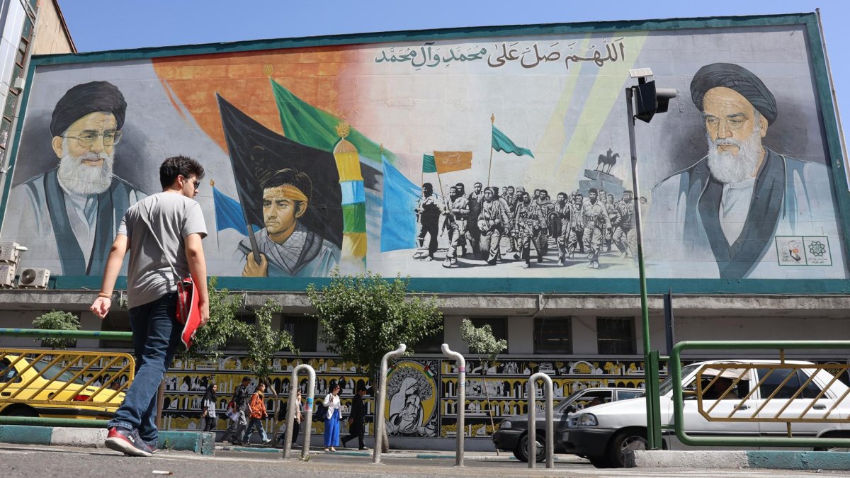 Iraníes caminan junto a una pintura mural del líder supremo iraní, el ayatolá Ali Jameneí (arriba-i) y el fallecido líder supremo iraní, el ayatolá Ruhollah Jomeiní, en una calle de Teherán.