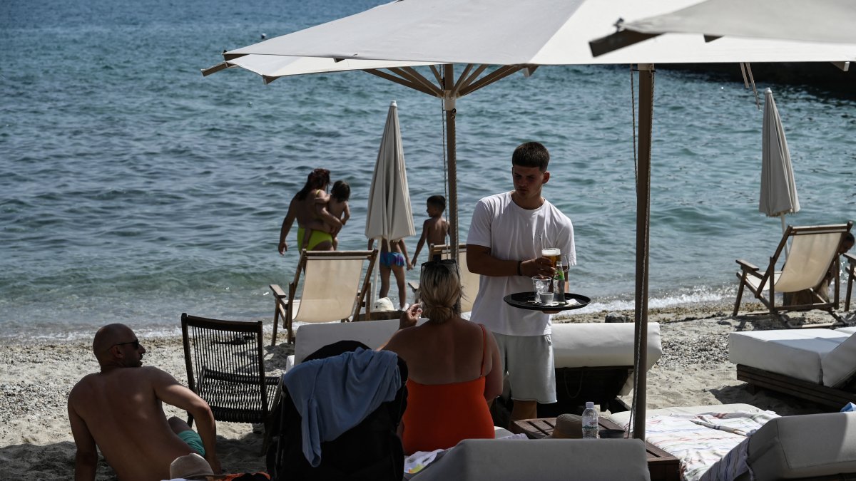 Un camarero sirve bebidas a los bañistas sentados en sus tumbonas a lo largo de la playa en la península de Halkidiki, en el norte de Grecia, en junio de 2025.