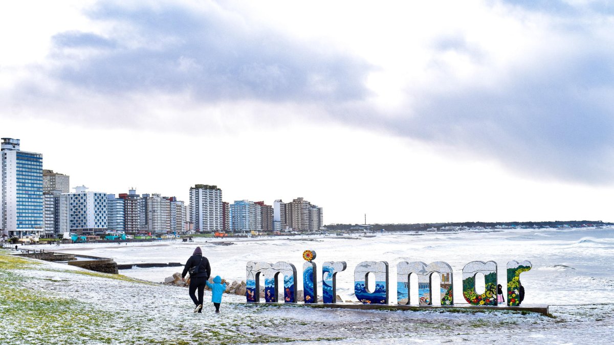 Personas caminan en una playa cubierta de nieve este lunes 30 de junio de 2025, en Miramar (Argentina).
