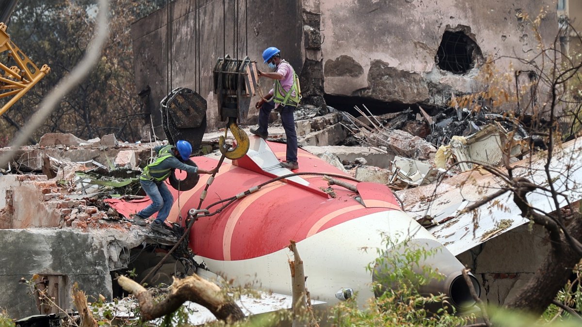 Fotografía del 14 de junio de 2025 que muestra a trabajadores indios que retiran los restos del avión de Air India con una grúa del lugar del accidente, cerca del aeropuerto de Ahmedabad.