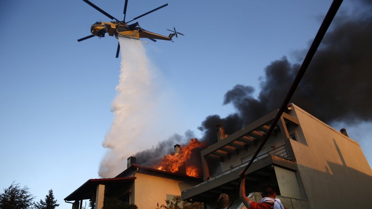 Un helicóptero de bomberos y voluntarios luchan para apagar un incendio que quema casas en la zona residencial de Kryoneri, en las afueras de Atenas, Grecia, este sábado 26 de julio.