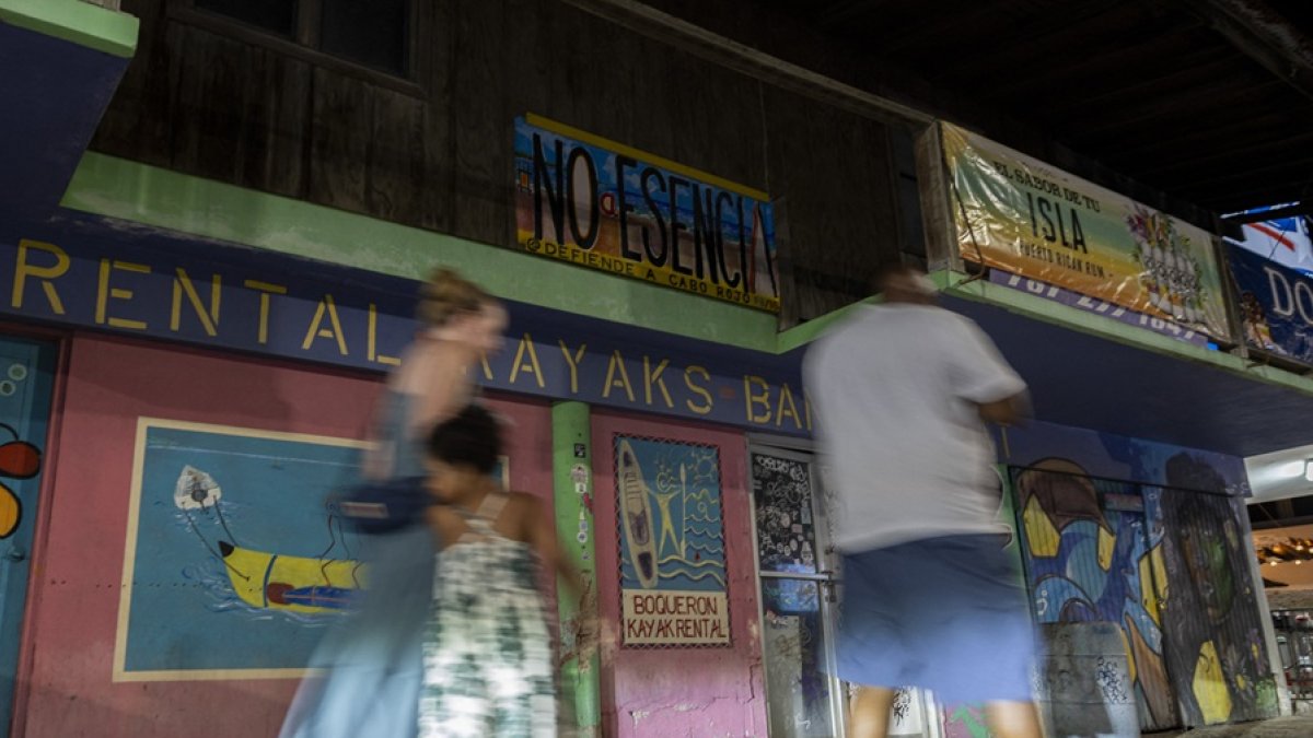 Personas pasan junto a un cartel en contra del proyecto Esencia en Cabo Rojo, Puerto Rico, el 15 de julio de 2025.