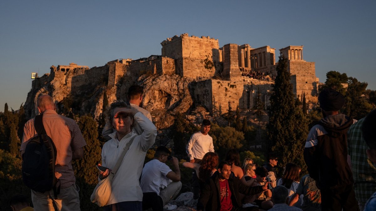 Los turistas disfrutan de una puesta de sol mientras están sentados en la colina del Areópago con vistas a la antigua Acrópolis de Atenas.