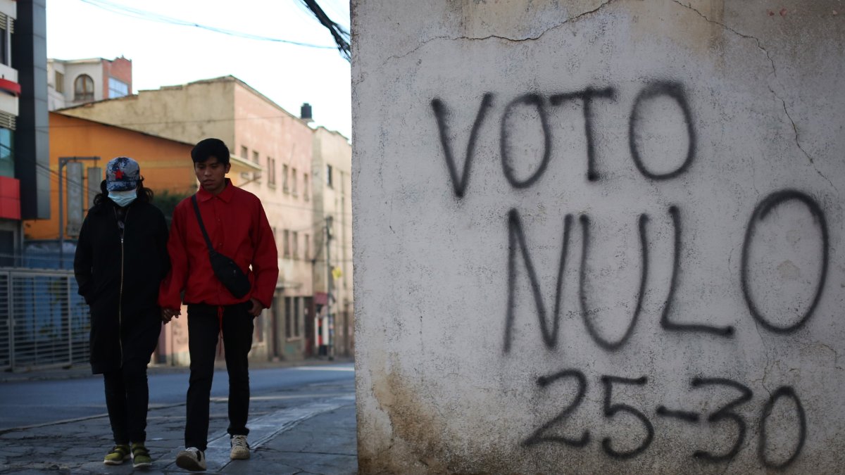 Personas caminan junto a un mural con un mensaje alusivo a la elecciones este sábado, en La Paz (Bolivia).