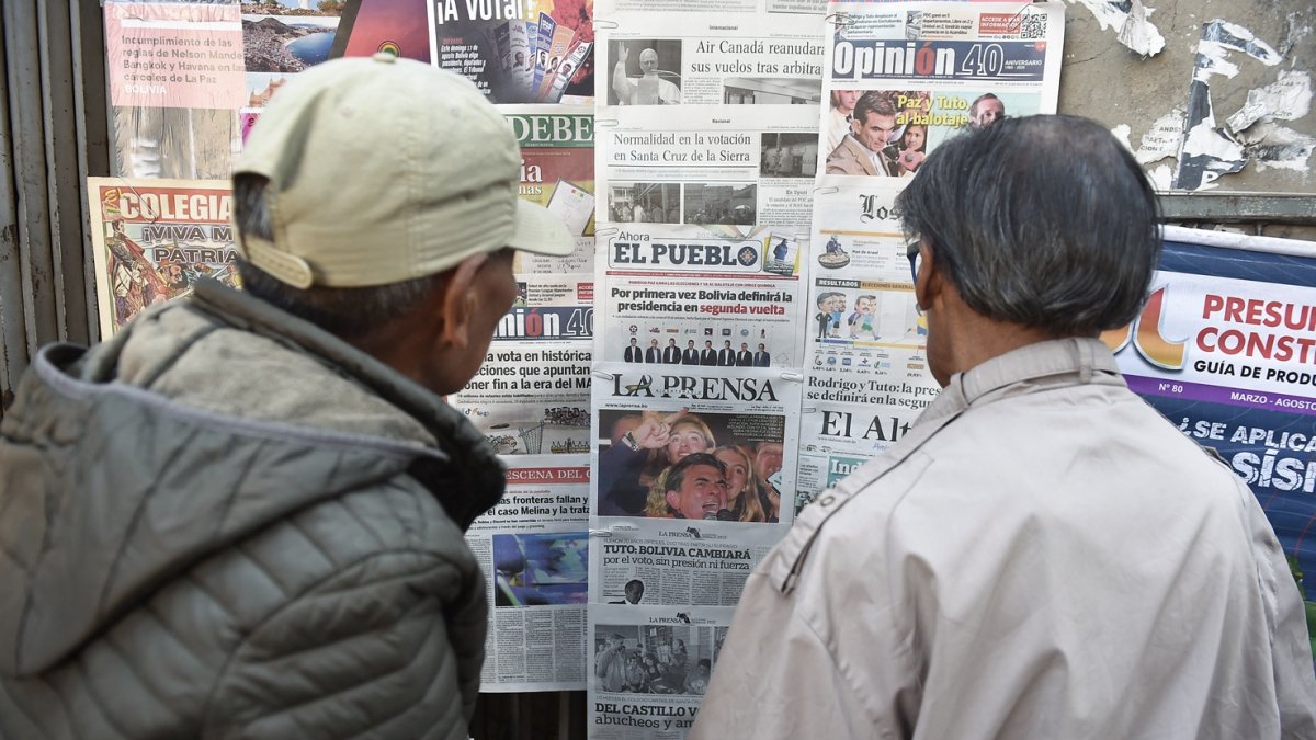 Dos personas leen periódicos con cobertura en portada de las elecciones presidenciales de Bolivia en un quiosco, en La Paz, el 18 de agosto de 2025.