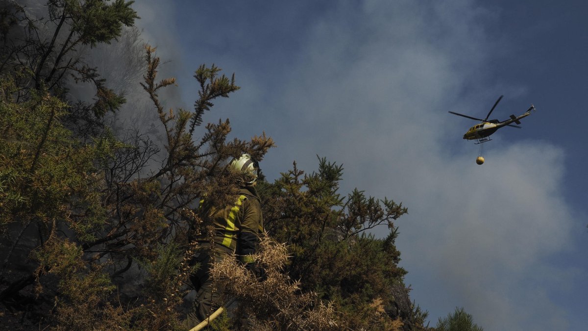 Un helicóptero de la lucha contra el fuego vuela sobre un bombero que trabaja en la extinción del incendio.(Lugo, Galicia).