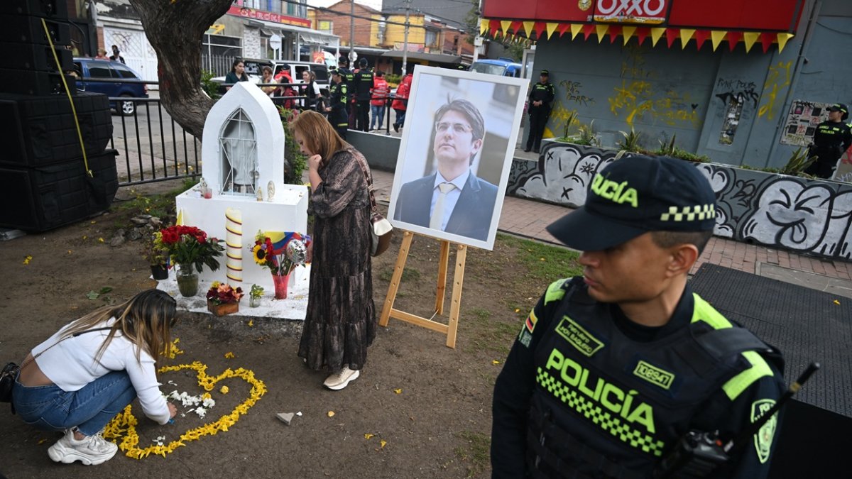 Las mujeres depositan flores junto a un retrato del candidato presidencial asesinado Miguel Uribe en el lugar donde le dispararon el 7 de junio en el barrio Modelia de Bogotá