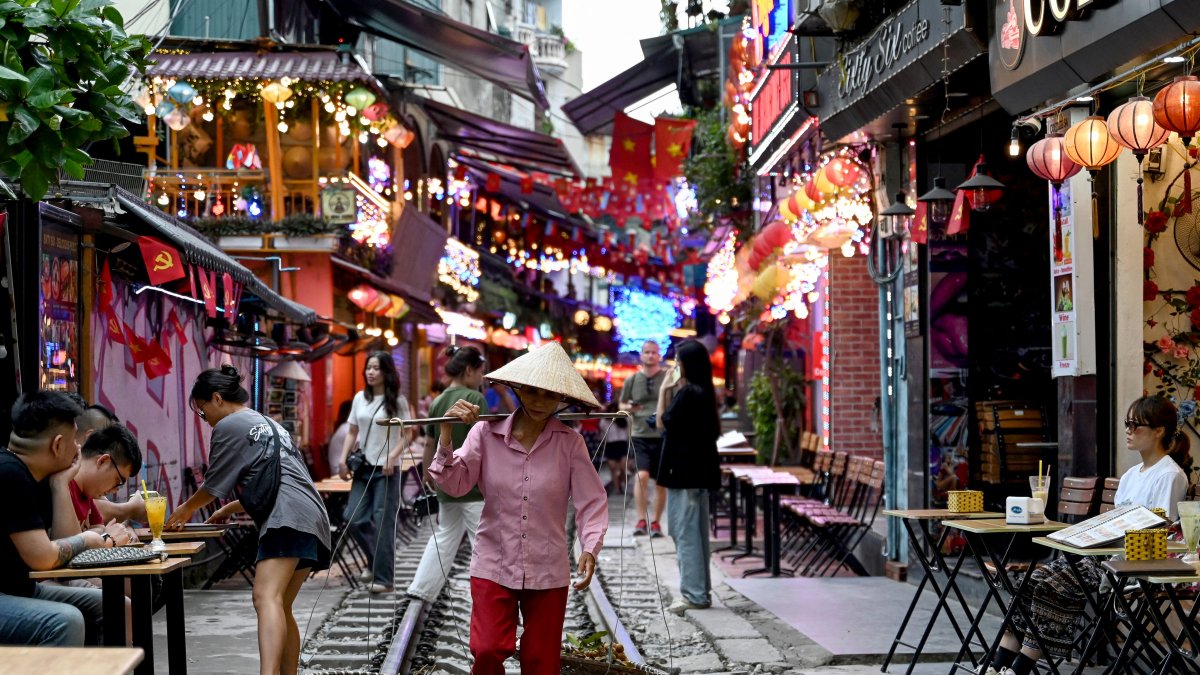 Turismo. Un vendedor ambulante caminando por una vía férrea entre terrazas de cafés en el centro de Hanói. Los turistas, disfrutan del lugar.