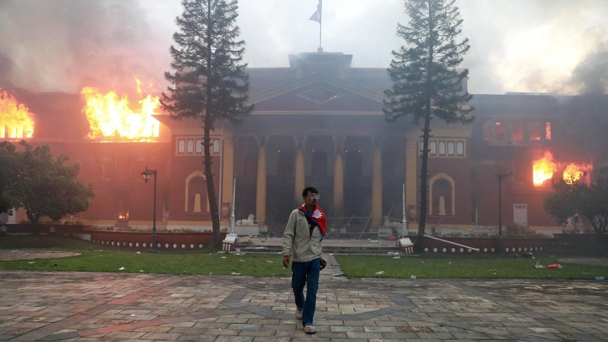 Un hombre está envuelto en la bandera nacional de Nepal mientras un incendio arrasa la oficina del presidente en Katmandú el 9 de septiembre de 2025.