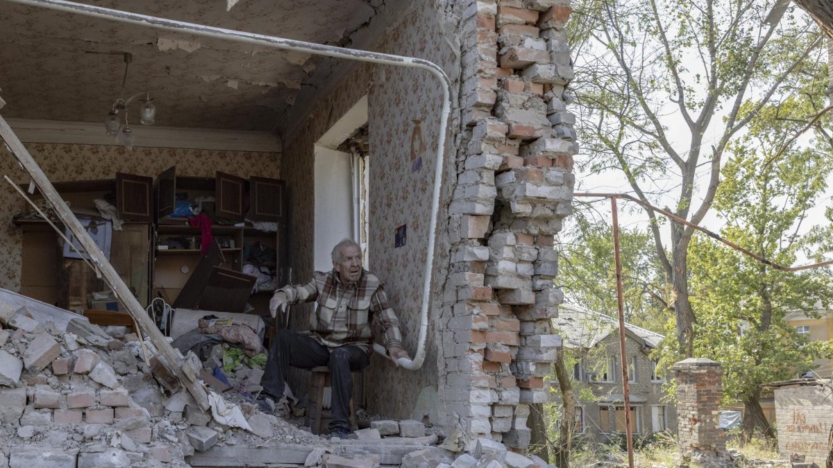 Un adulto mayor sentado entre los escombros de un edificio dañado, mientras los miembros de los