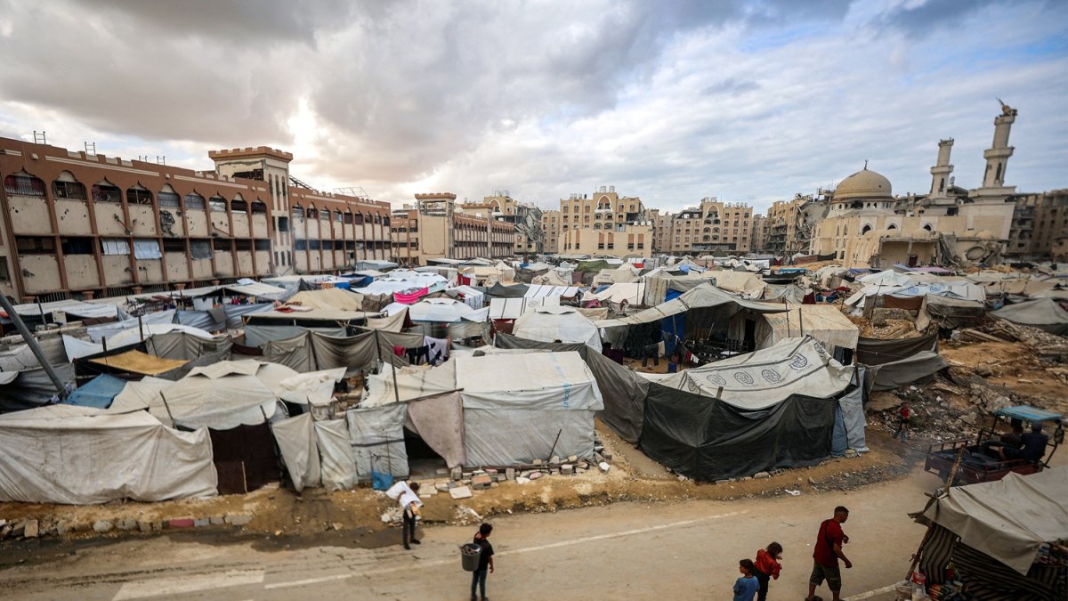 Un hombre y niños caminan junto a tiendas de campaña que albergan a personas desplazadas por la guerra, instaladas cerca de la mezquita Sheikh Hamad bin Khalifa Al-Thani, gravemente dañada.