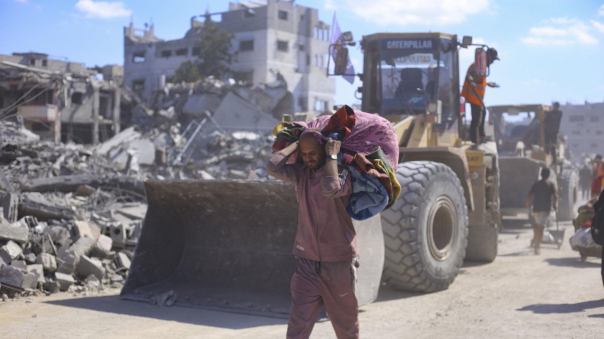 Un hombre con un hatillo con sus pertenencias pasa ante varias excavadoras en la ciudad de Gaza, que comienza este 14 de octubre de 2025 las operaciones de remoción de escombros.