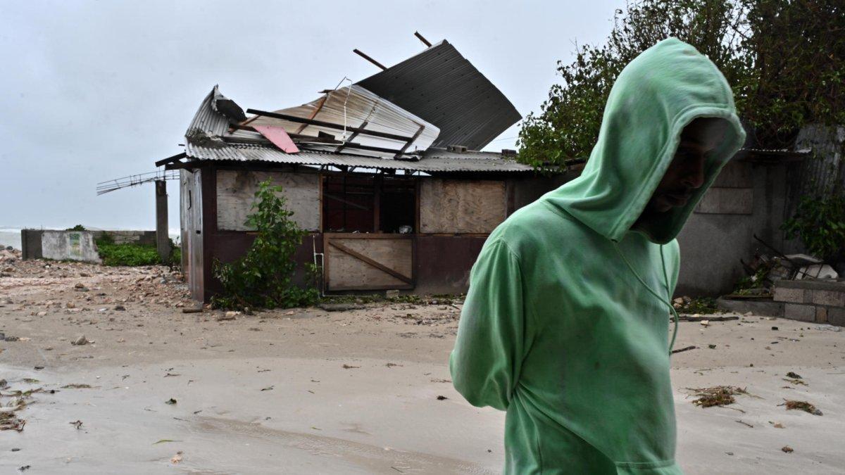 Una persona camina frente a una casa afectada por los vientos preliminares del huracán Melissa, en la playa pesquera de Hellshire, en Portmore (Jamaica).