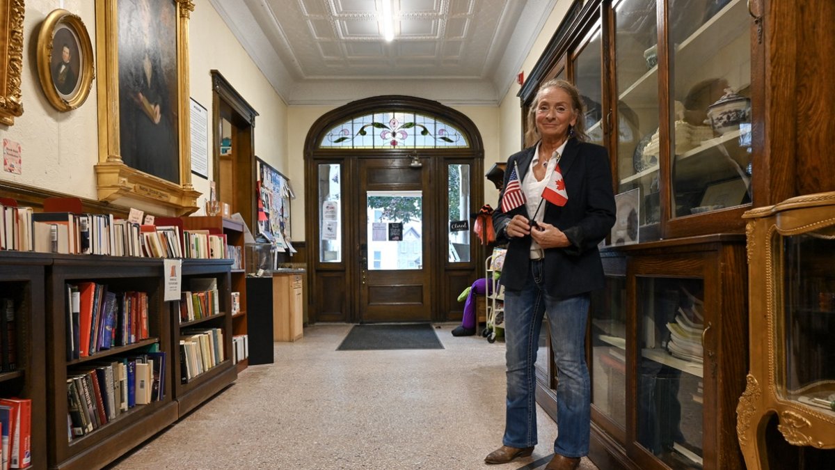 Sylvie Boudreau, presidenta de la junta directiva de la biblioteca transfronteriza Haskell, posa sobre el marcador negro que indica los lados de EE. UU. (izq.) y Canadá, dentro de la biblioteca.