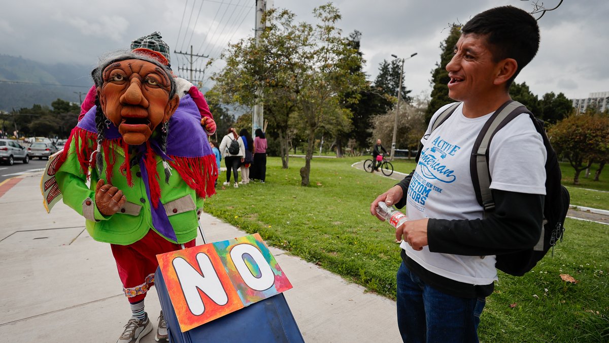 Una persona disfrazada sostiene una maleta mientras un hombre lo observa durante una manifestación contra el referéndum en Quito (Ecuador).