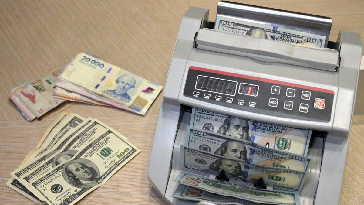 Una ilustración muestra una máquina contando billetes de pesos argentinos junto a billetes de dólares estadounidenses en Buenos Aires el 22 de octubre de 2025.