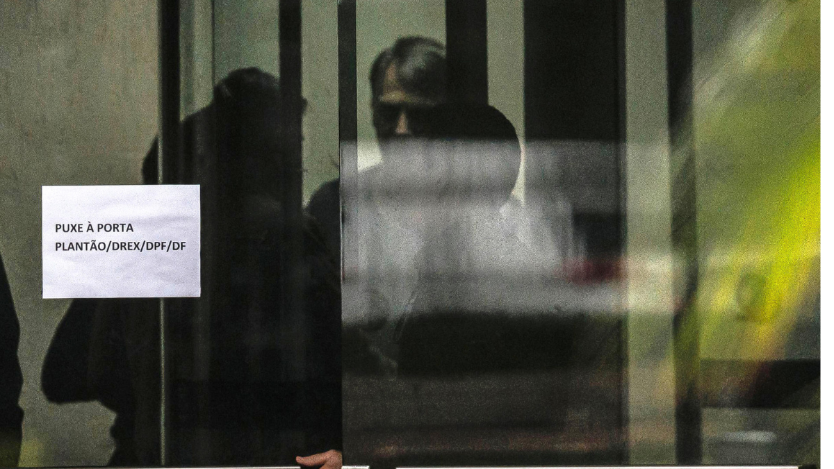 Bolsonaro aparece tras una puerta en la Policía Federal de Brasilia, donde explicó que quemó su tobillera electrónica tras sufrir “paranoia” por medicamentos.