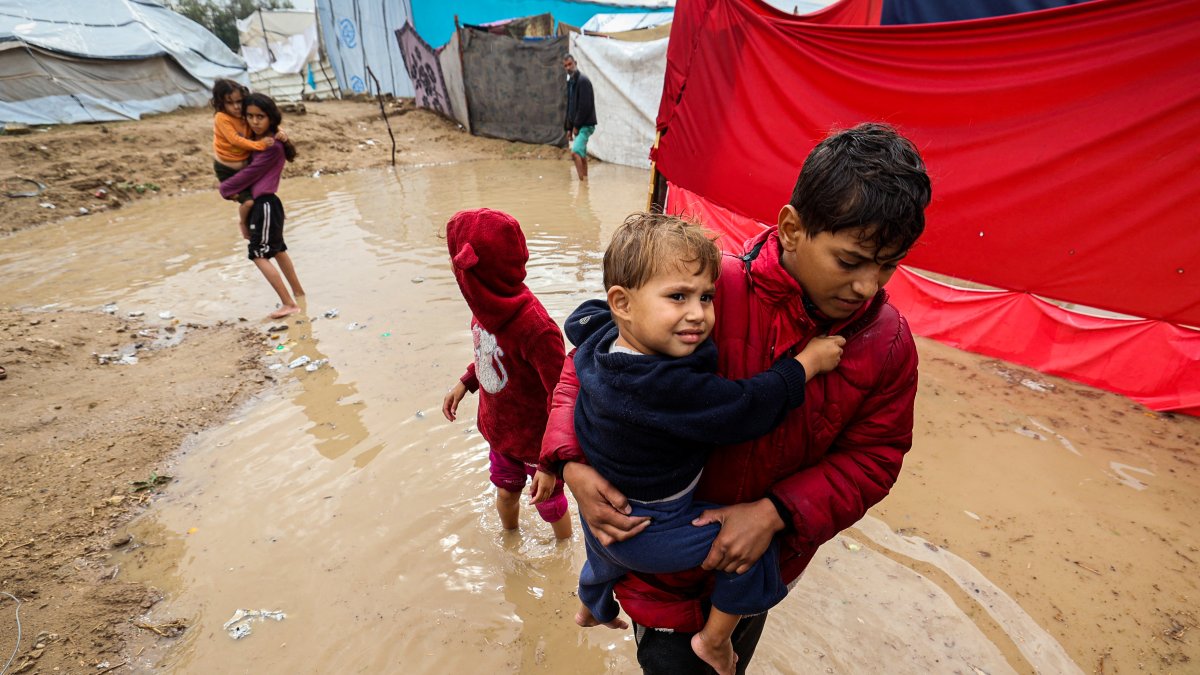 Niños palestinos caminan entre aguas inundadas tras fuertes lluvias en un campamento.