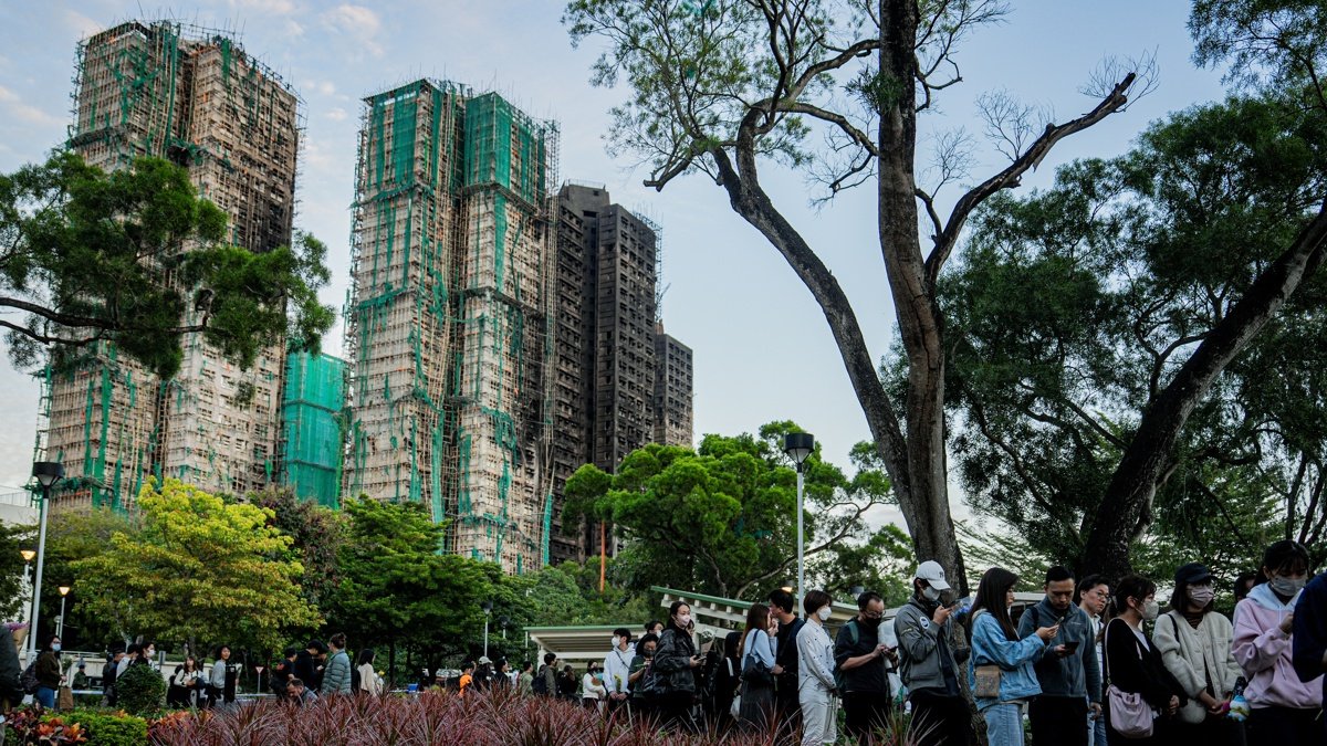 Varias personas dejan flores como tributo a las víctimas del incendio del complejo residencial Wang Fuk Court, en el fondo.