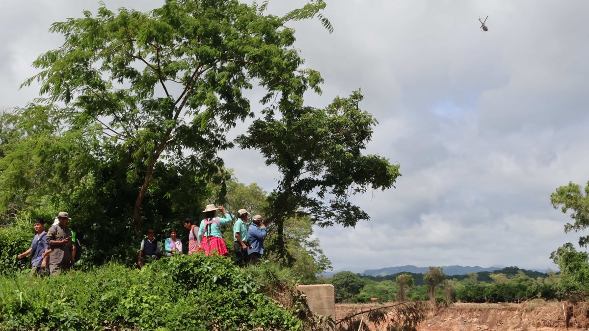 Personas observan una zona afectada por el desbordamiento de un río este domingo 14 de diciembre, en El Torno (Bolivia).