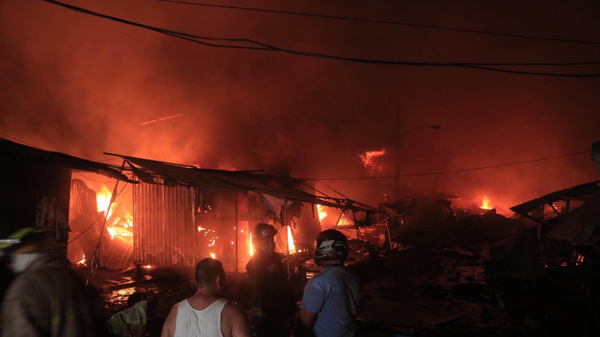 Cuerpo de Bomberos de Honduras trabajan junto a ciudadanos para controlar un incendio provocado en un puesto de venta de pólvora en San Pedro Sula (Honduras).