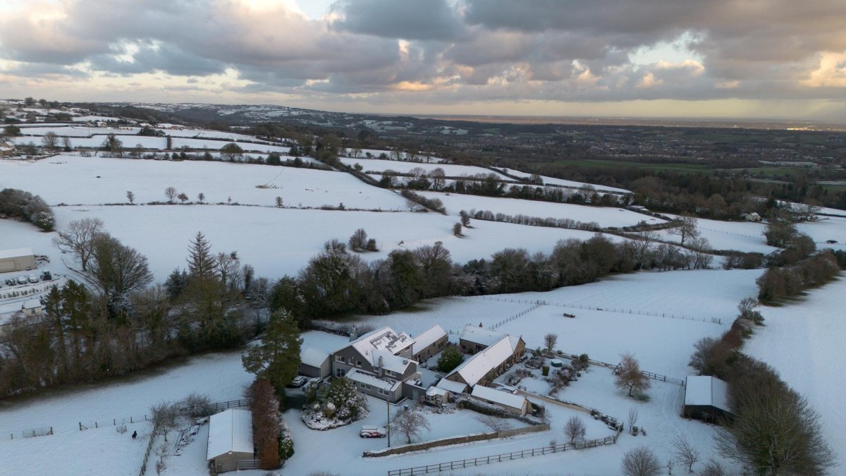 La imagen muestra un paisaje rural cubierto de nieve y edificios agrícolas en el Reino Unido durante una importante ola de frío a inicios de 2026.