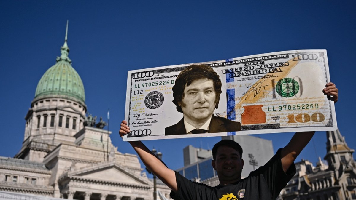 Un partidario del presidente Javier Milei, muestra un cartel de un billete de cien dólares con la imagen del presidente afuera del Congreso.