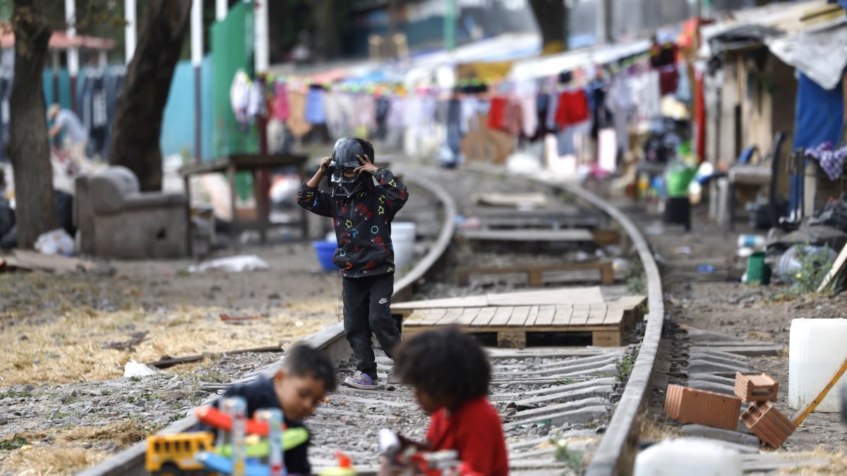 Hecho. Menores migrantes juegan sobre la vía de un campamento, en Ciudad de México (México), entre muros de madera, lonas y otros materiales reciclados.