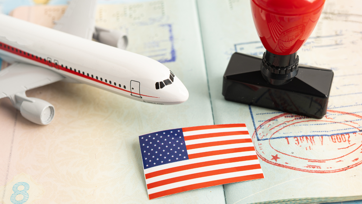 Referencial. Pasaporte con sellos de entrada y salida, junto a una bandera de EE.UU. y un avión en miniatura, simboliza las tensiones migratorias entre Tailandia y Estados Unidos.