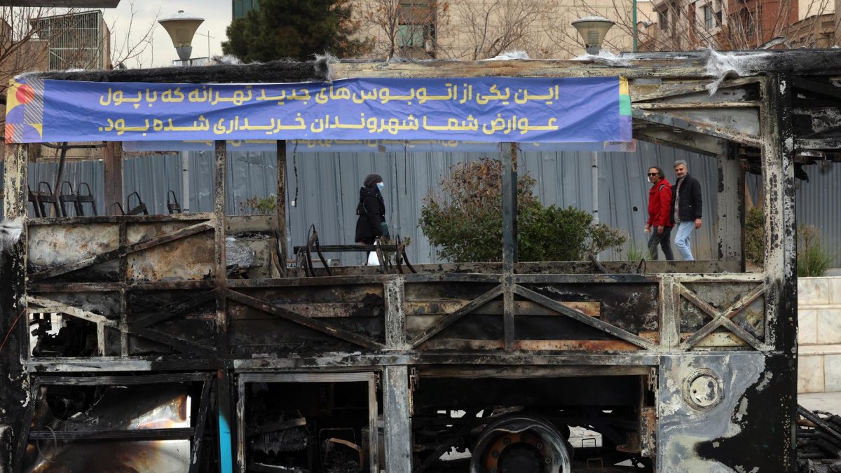 Iraníes caminan cerca de los restos de un autobús público incendiado en Teherán, Irán, el 15 de enero de 2026.