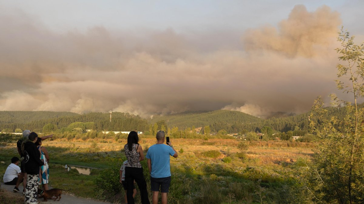 Personas observan el humo tras incendios forestales este domingo, en la comuna de Penco, Concepción (Chile).
