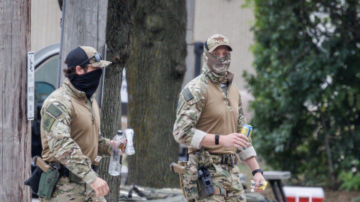 Agentes enmascarados del Servicio de Inmigración y Control de Aduanas (ICE) caminando frente a la entrada del centro de detención (Estados Unidos).