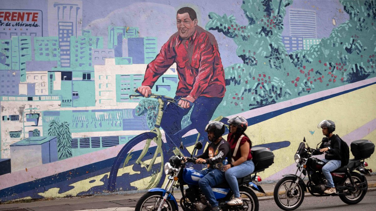 Motociclistas transitando frente a un mural del fallecido presidente de Venezuela, Hugo Chávez, este lunes 2 de febrero de 2026, en Caracas (Venezuela).