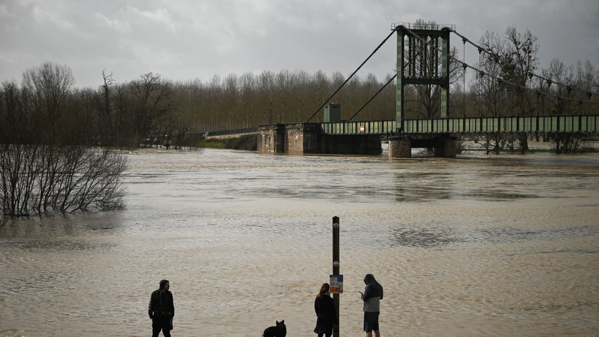 Personas en un sendero rodeado de una zona inundada en Marmande, suroeste de Francia, el 12 de febrero de 2026, mientras la tormenta Nils provoca inundaciones excepcionales a lo largo del río Garona.