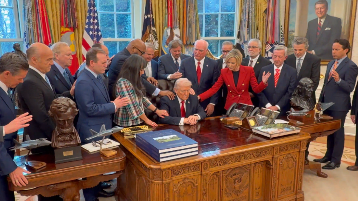 Donald Trump aparece sentado detrás de su escritorio, mientras un grupo de pastores evangélicos coloca sus manos sobre él y eleva una oración.