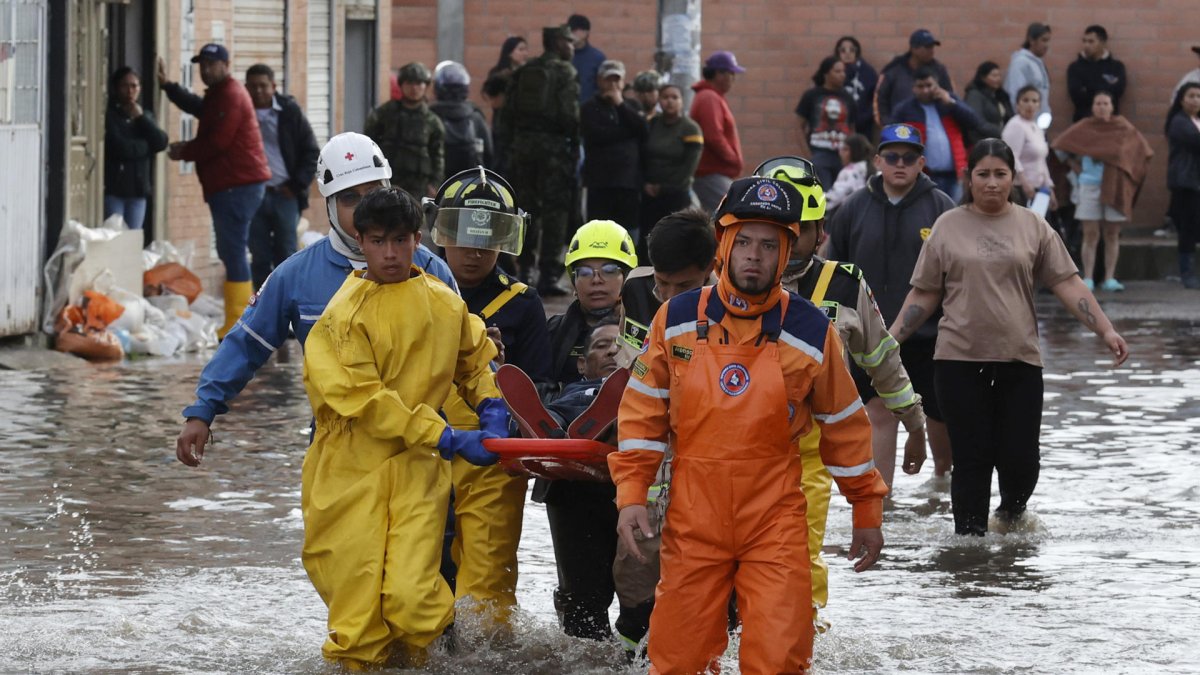 Integrantes de organismos de rescate socorren a un hombre en una calle inundada por fuertes lluvias este jueves, en Facatativá (Colombia).