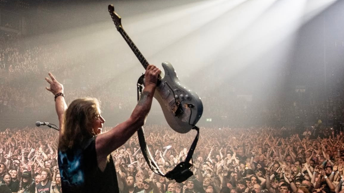 Integrante de Iron Maiden levanta su guitarra ante miles de fanáticos durante un concierto, en una escena que refleja la energía de la banda británica en vivo.