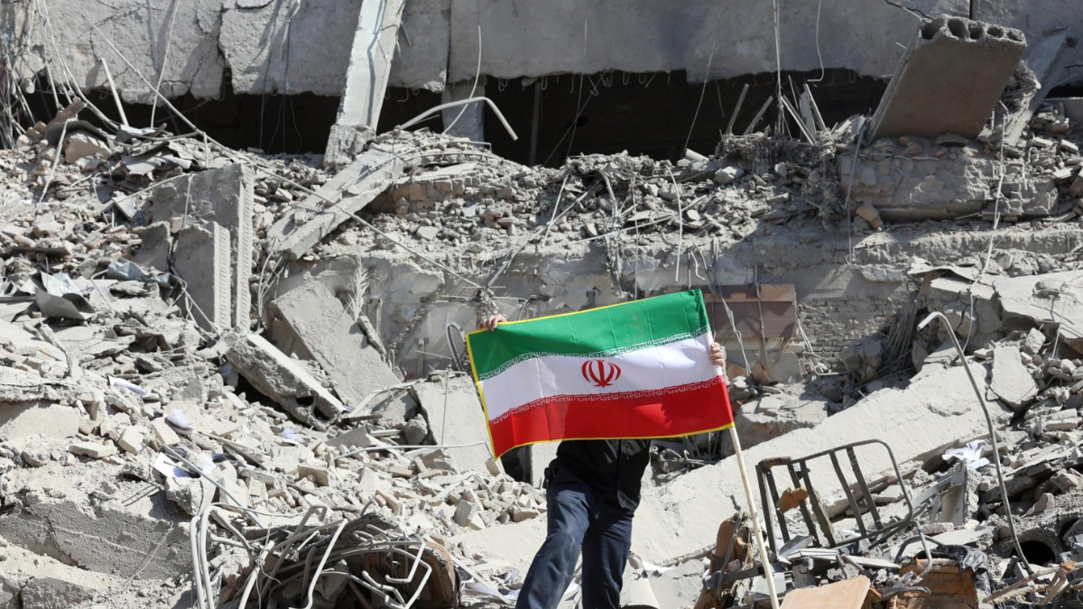 “Un ciudadano sostiene la bandera de Irán en medio de los escombros tras recientes ataques.
