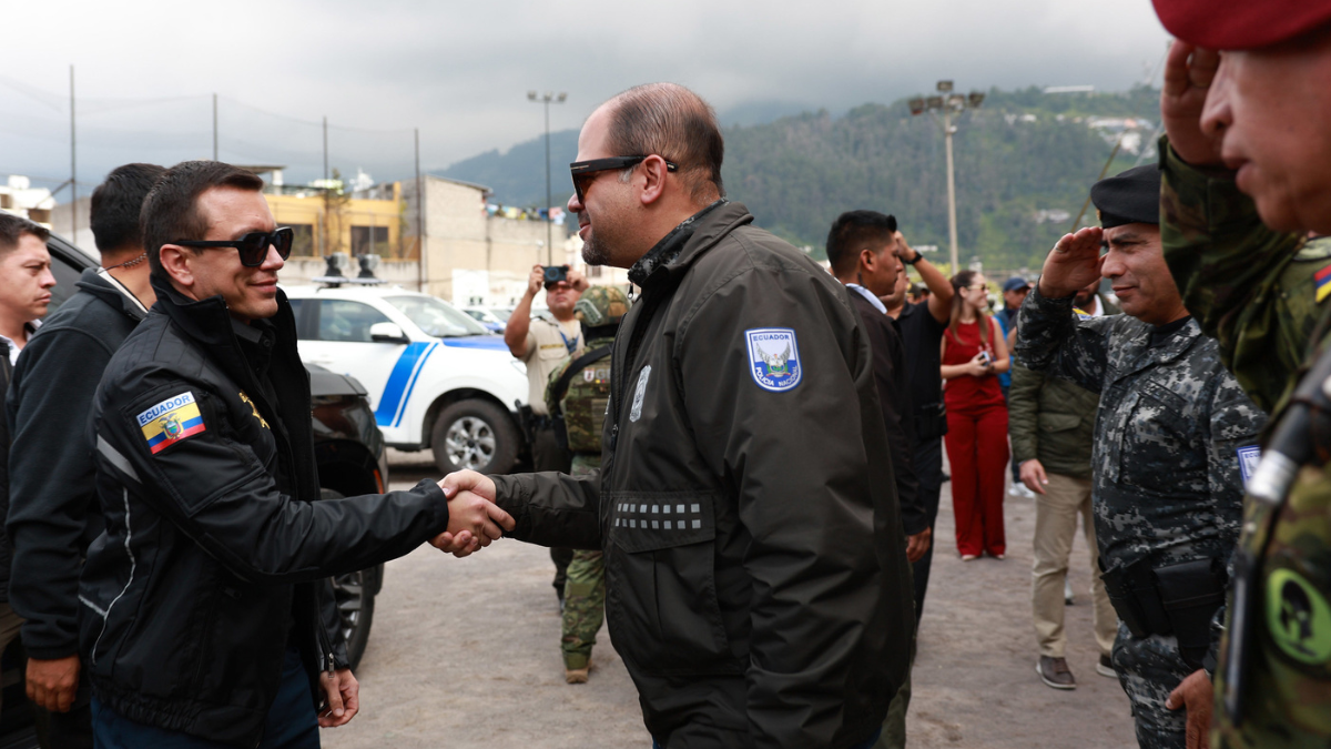 El presidente Daniel Noboa estrecha la mano del ministro del Interior, John Reimberg, durante un acto oficial acompañado por personal militar.