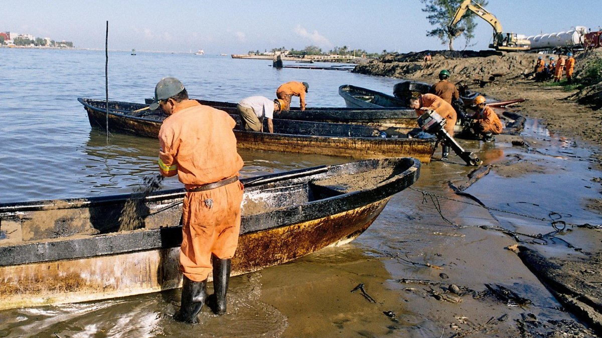 Fotografía de referencia de trabajadores petroleros contratados por la paraestatal Petróleos Mexicanos que limpian en una zona de un derrame de crudo.