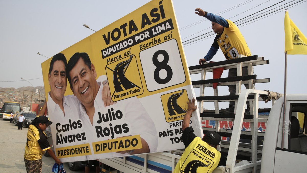 Personas sostienen una valla publicitaria del candidato a la Presidencia de Perú Carlos Álvarez y el diputado Julio Rojas este sábado, en Lima (Perú).