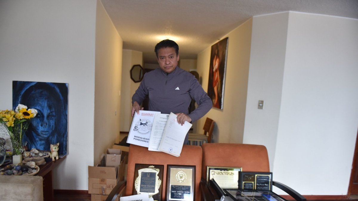 Jonnathan Carrera con varias  fotos y placas de los reconocimientos que recibió su padre por el aporte para dar identidad, normativa y masificación del ecuavóley.