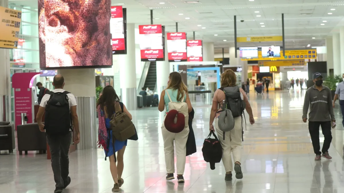 Personal aeroportuario y viajeros se movilizan hacia la terminal aérea con documentación de vuelo en medio de las restricciones nocturnas.