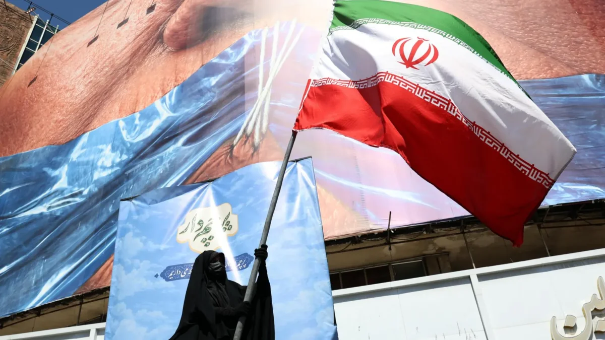 Una mujer con velo sostiene la bandera nacional de Irán frente a una enorme valla publicitaria antiestadounidense en Teherán, Irán, el 11 de mayo de 2026.