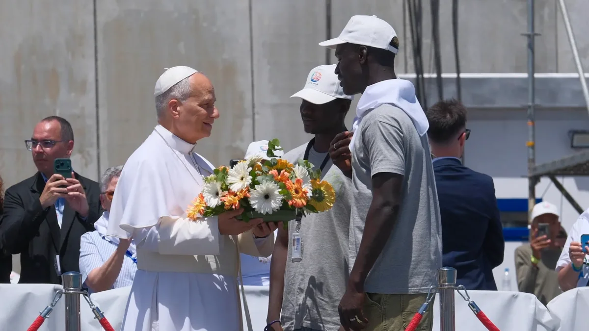 El papa León XIV recibe flores de dos voluntarios para protagonizar una ofrenda floral en el mar en recuerdo de los migrantes muertos.