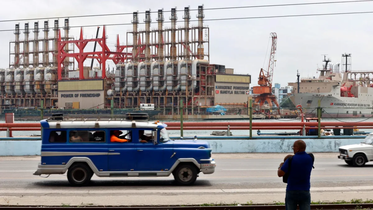Un auto viejo de transporte colectivo al pasar frente a una planta flotante de generación eléctrica en el puerto de La Habana (Cuba).